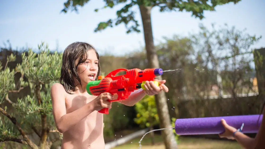 Barn springer genom en sprinklermatta i solen